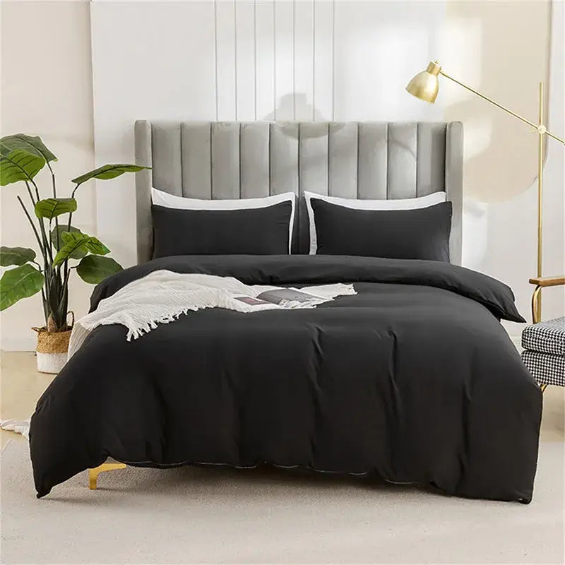 Black satin duvet cover set with matching pillowcases displayed on bed with tufted gray headboard for soft bedding cover set