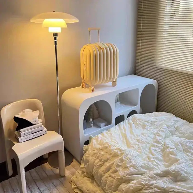 Cream-colored ribbed hard-shell suitcase with gold-tone wheels and handle shown alongside retro black glass shade led floor lamp