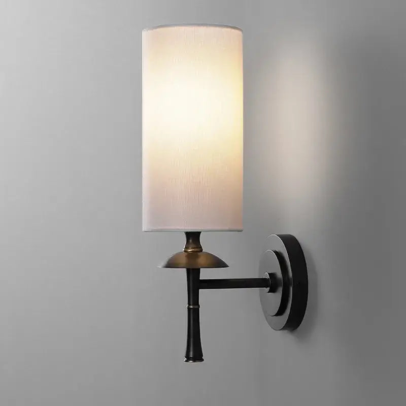 A sleek retro black metal brass wall lamp with a cylindrical off-white fabric shade for bedroom decorbites brass wall lamp