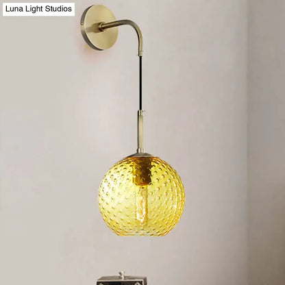 A warm amber glass globe pendant light with textured bubble surface and brass hardware for pink yellow blue decor