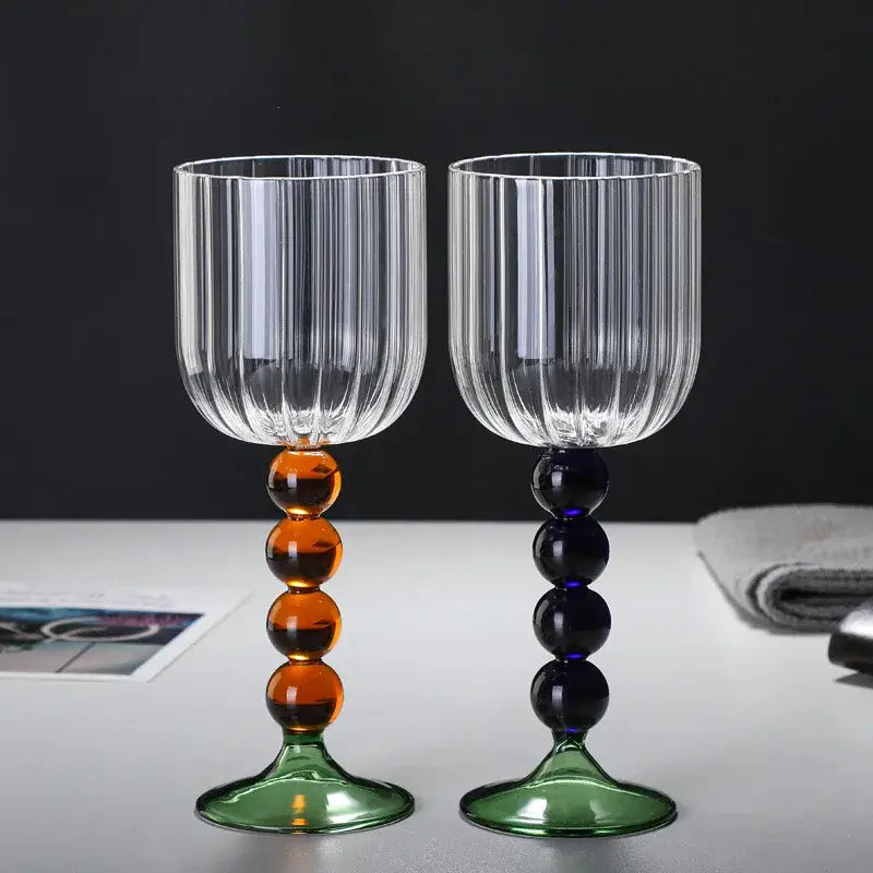 A pair of clear ribbed wine glasses with colorful glass twister stems in amber and deep blue on green bases