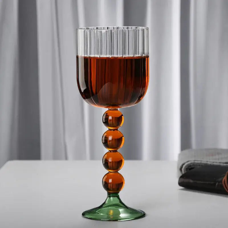 A tall elegant wine glass twister with clear ribbed bowl amber glass twister stem and green base for dining room use
