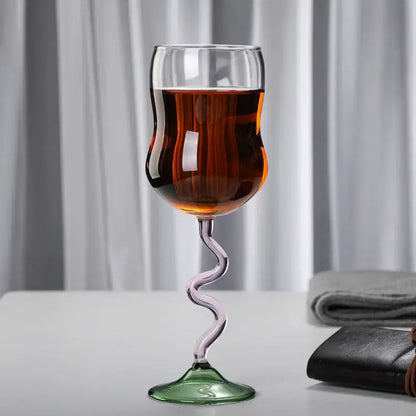 A clear glass wine glass twister with a blue and green ribbed stem filled with amber liquid for dining use