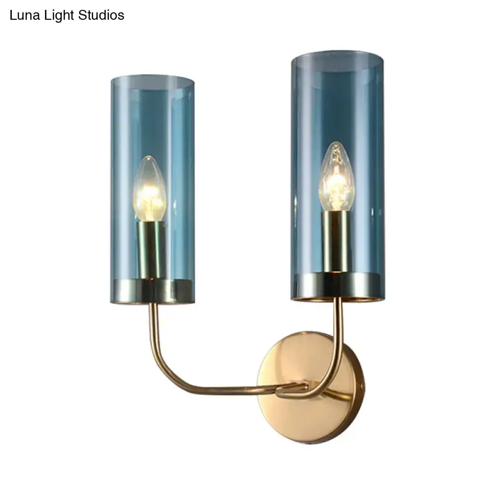 Blue-tinted glass cylinder wall mount lamp with brass-finished metal arms for living room use