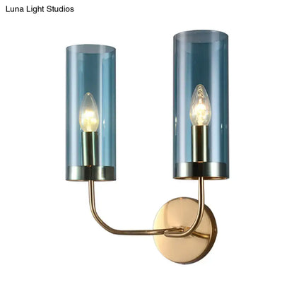 Blue-tinted glass cylinder wall mount lamp with brass-finished metal arms for living room use