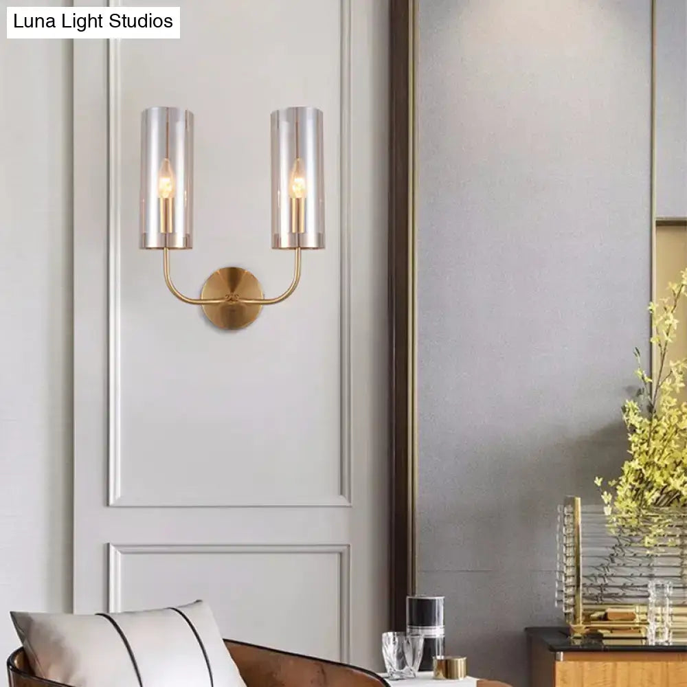 Gold-toned retro brass wall mount lamp with two cylindrical smoked glass shades and a curved arm for living room use