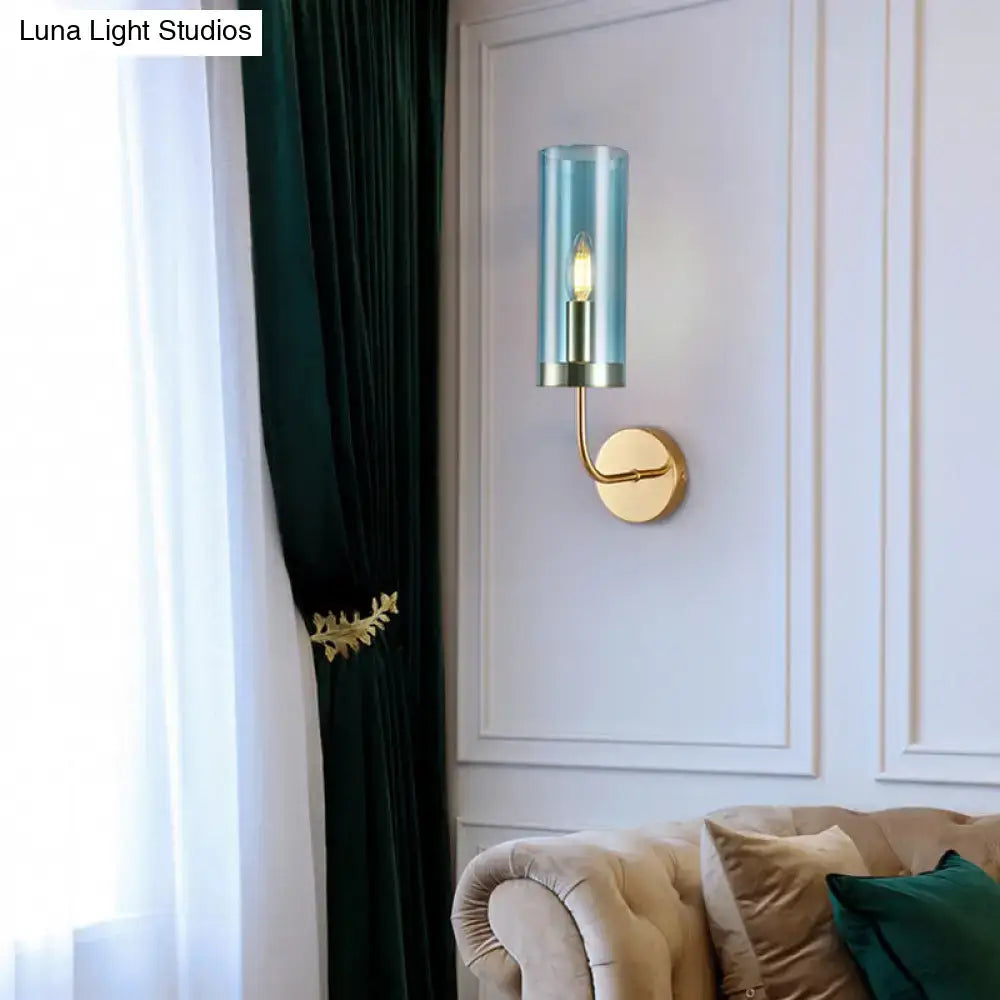 A sleek cylindrical retro brass wall mount lamp with a translucent teal glass shade for living room use