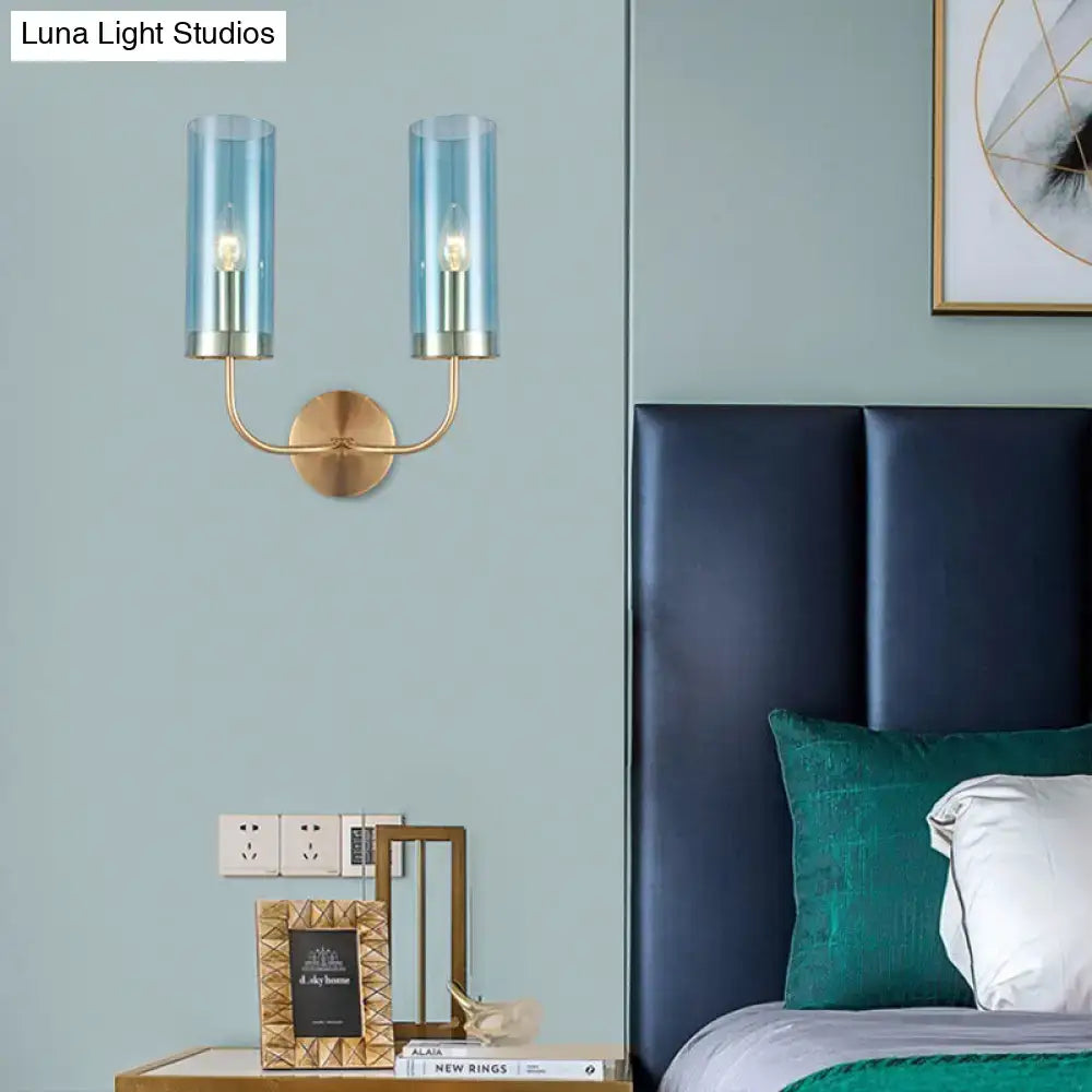 Retro brass wall mount lamp with blue-tinted glass cylinder shade and brass-finished metal arms for living room use