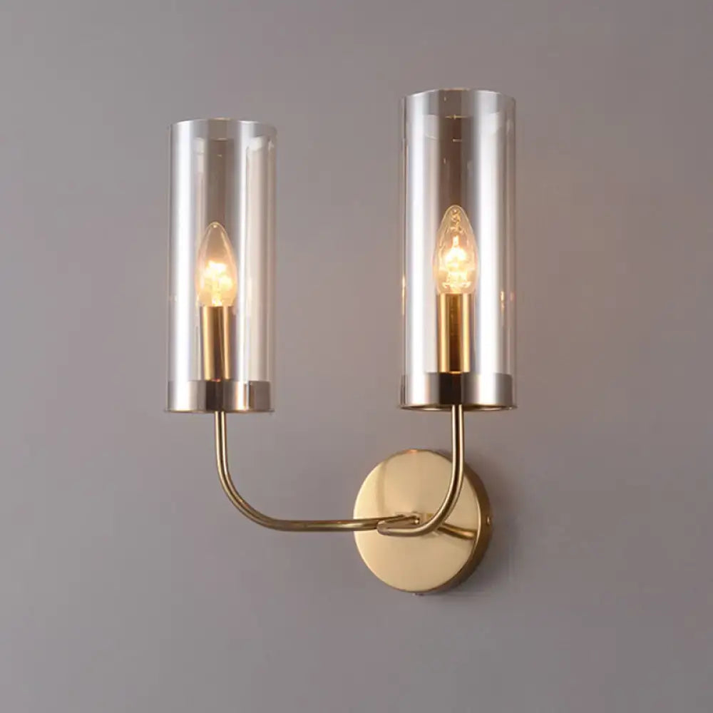 Modern brass wall mount lamp with two cylindrical smoked glass shades housing warm-toned bulbs for living room use