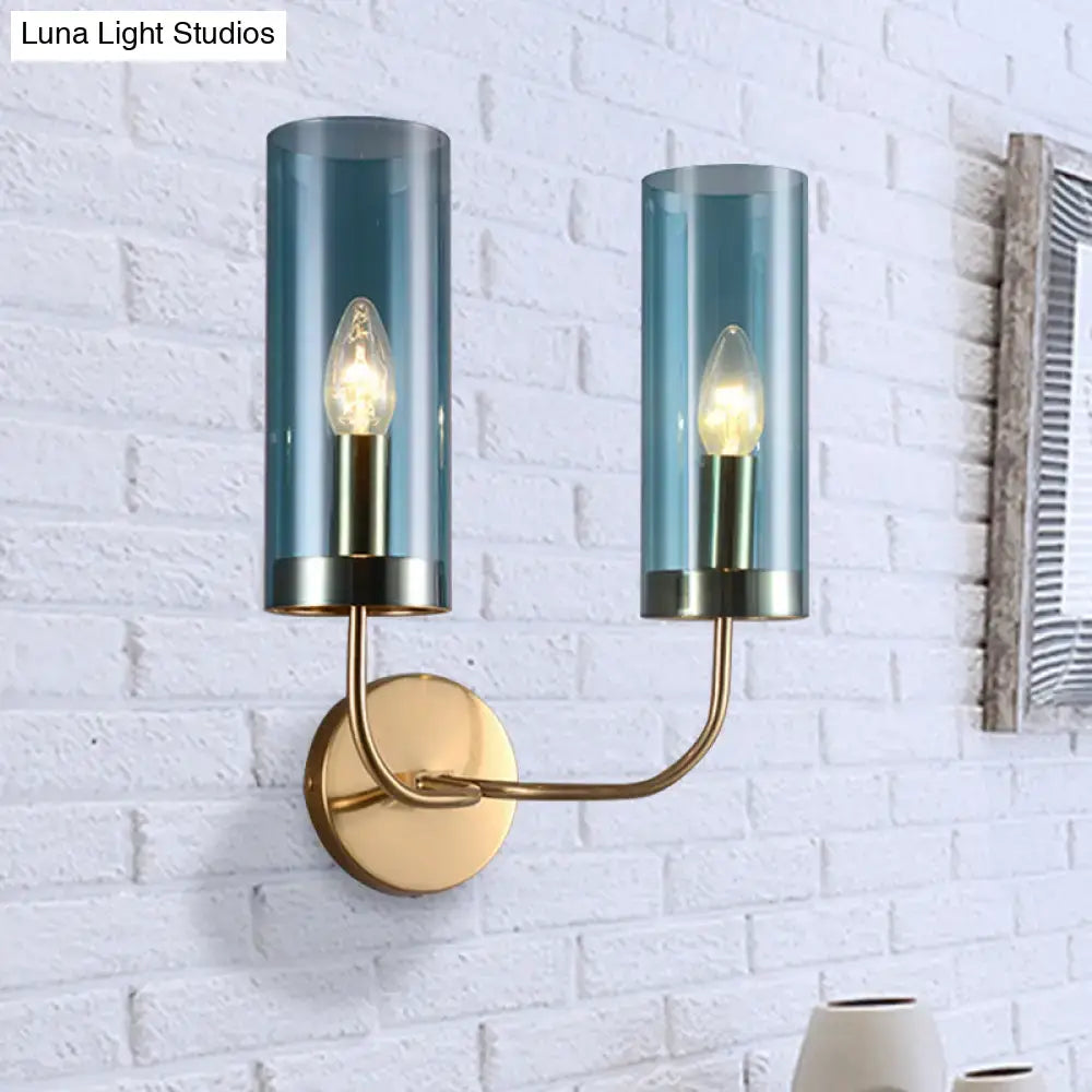 Modern brass wall mount lamp with two teal smoked glass cylinders housing warm bulbs for living room use