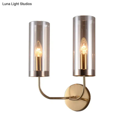 Modern brass-finished wall mount lamp with two cylindrical smoked glass shades housing warm filament bulbs for living room use