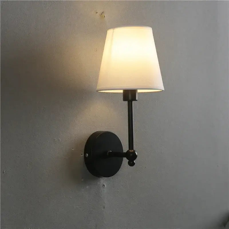 Black wrought iron wall lamp with cream fabric shade designed as a gold led retro style bedroom sconce