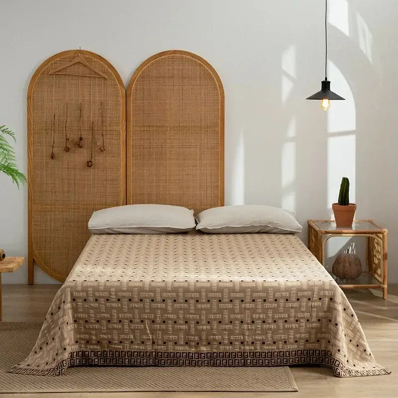 Beige decorbites cotton throw blanket with geometric pattern and dark brown border draped over bed with rattan headboards