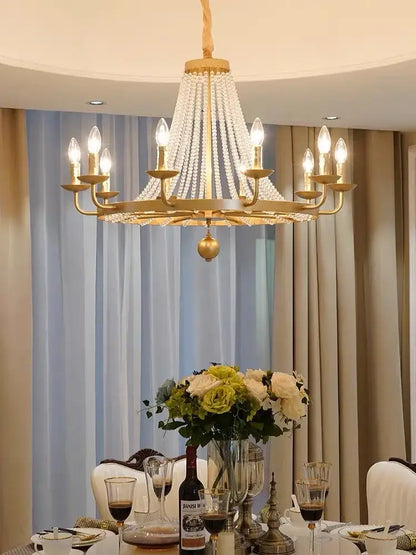 Gold-toned decorbites crystal chandelier with cascading crystal strands and lit candle bulbs for dining room decor