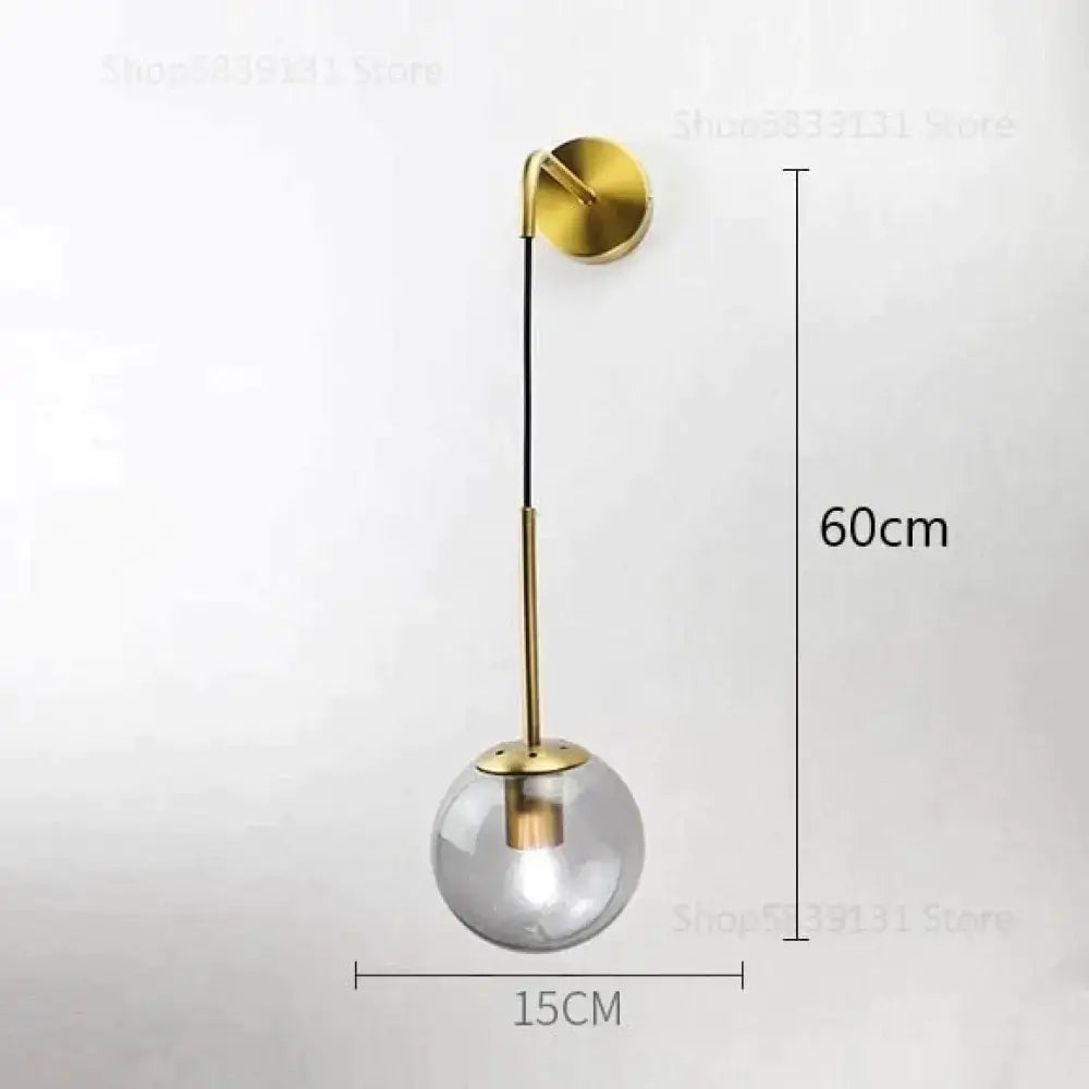 A modern brass-finished wall lamp with a clear glass globe and slender stem for nordic retro modern bedroom lighting