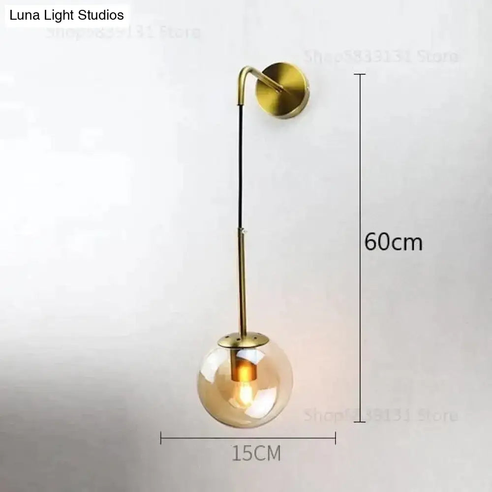 A modern brass wall lamp with a slender curved arm and smoked amber glass globe for Nordic retro modern bedroom lighting