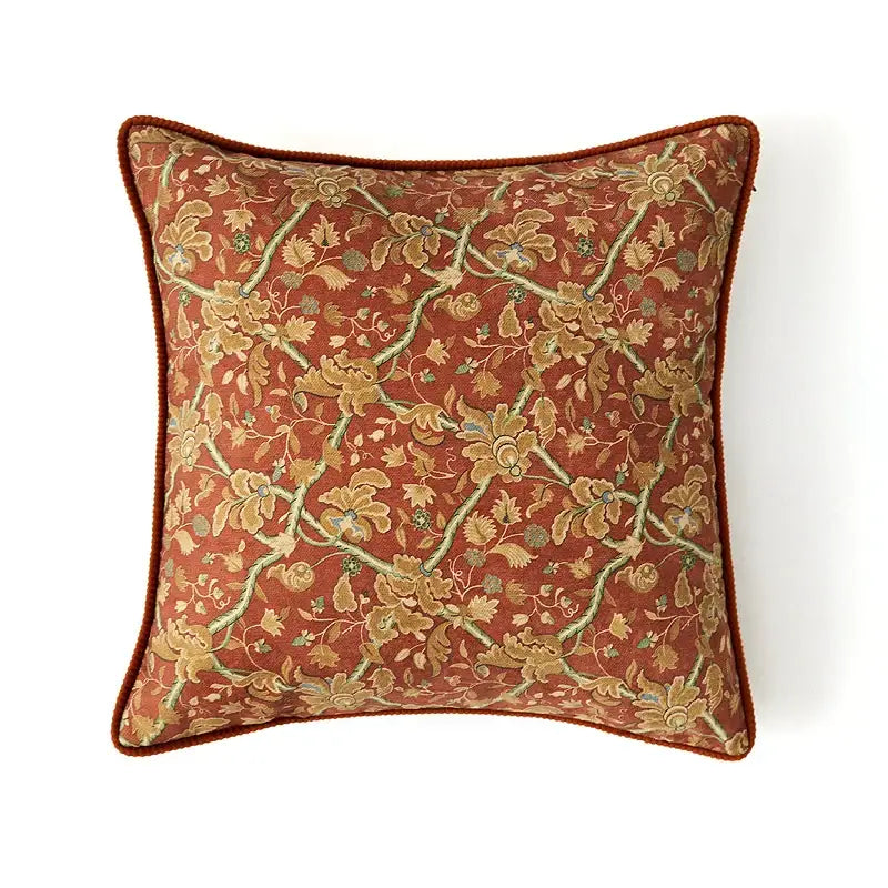 A rust-colored square cushion cover with intricate gold green floral pattern and corded border by decorbites American Luxe