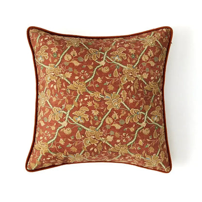 A rust-colored square cushion cover with intricate gold green floral pattern and corded border by decorbites American Luxe