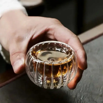 A ribbed clear double wall glass teacup set holding amber tea with a delicate fluted design for dining room use