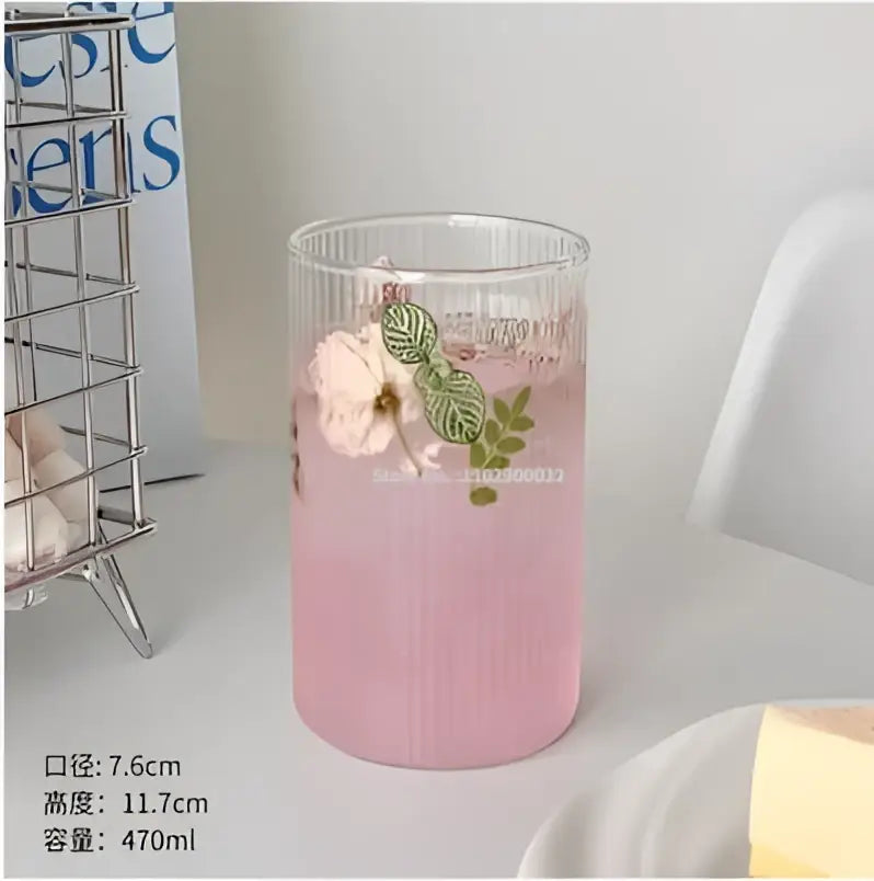 Ribbed clear glass coffee cup tumbler filled with pink liquid and garnished with green leaves and a white flower decorbites clear glass