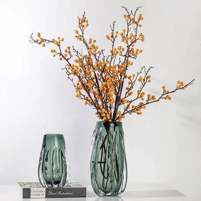 A tall ribbed emerald green decorbites crystal vase with modern design holds orange berry branches for living room decor