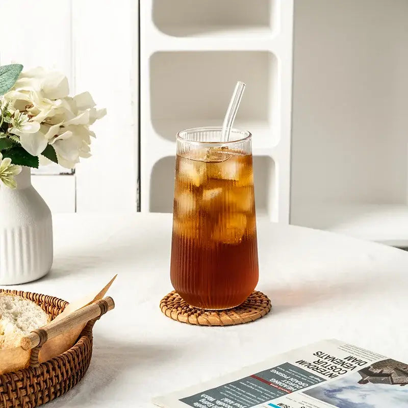 Tall ribbed frosted and clear glass coffee cup with iced tea and clear straw on woven coaster by decorbites clear glass cups