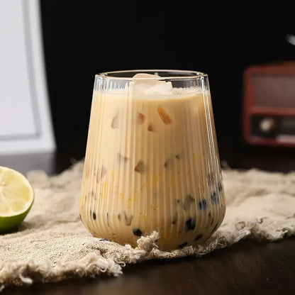 A clear ribbed glass cup filled with creamy iced coffee and black tapioca pearls from a glass cup set with bamboo lid and straw