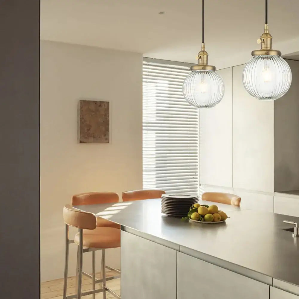 Brass-finished pendant light with ribbed glass globe hanging above a modern kitchen island decorbites clear glass