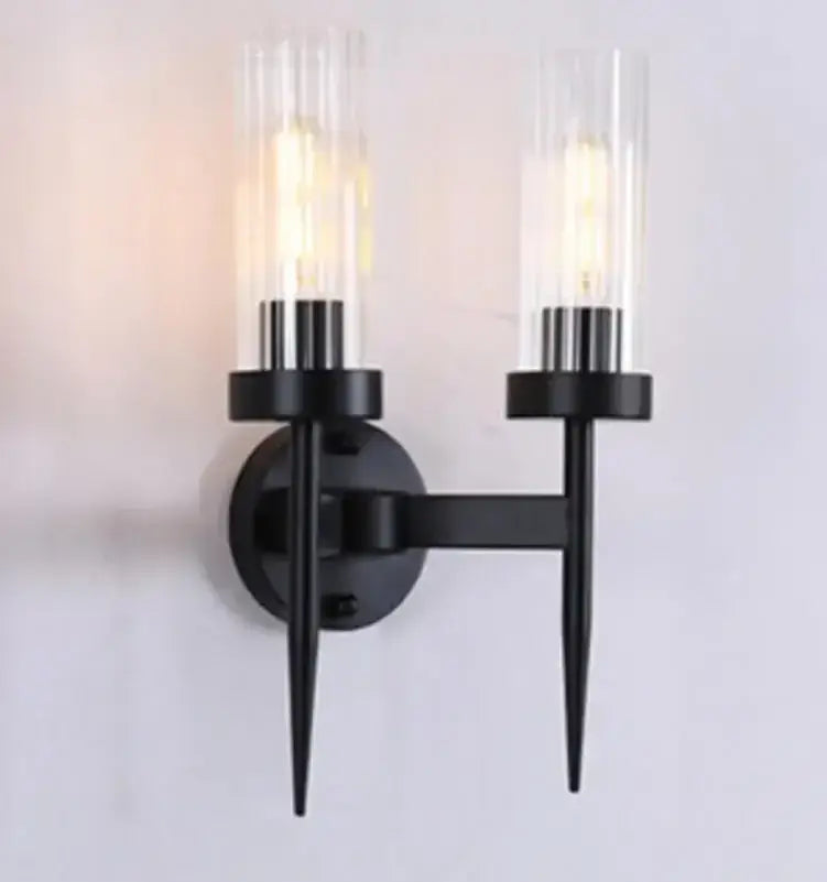 Black metal wall lights with two clear ribbed glass cylinders and warm decorbites gold led bulbs for bedroom decor