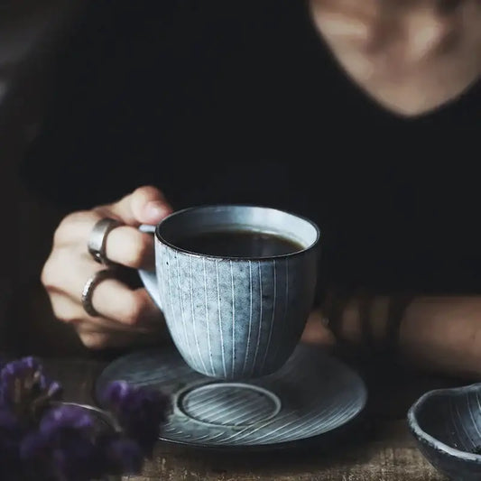 A matte gray ribbed ceramic coffee cup with matching saucer from a ribbed matte gray ceramic coffee cup set