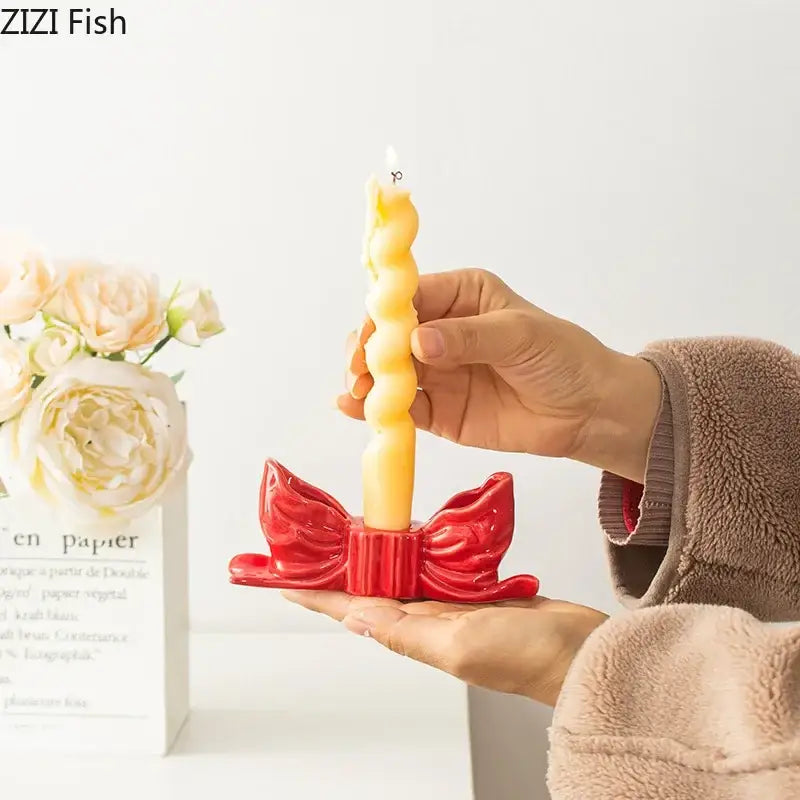 A vibrant red ceramic bowknot candle holder with ribbed design holding a twisted yellow wax candle for decorbites desk decor