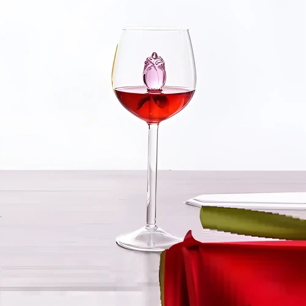 A clear rose stemware wine glass with red liquid and a pink crystal owl decorbites 3d rose floating inside