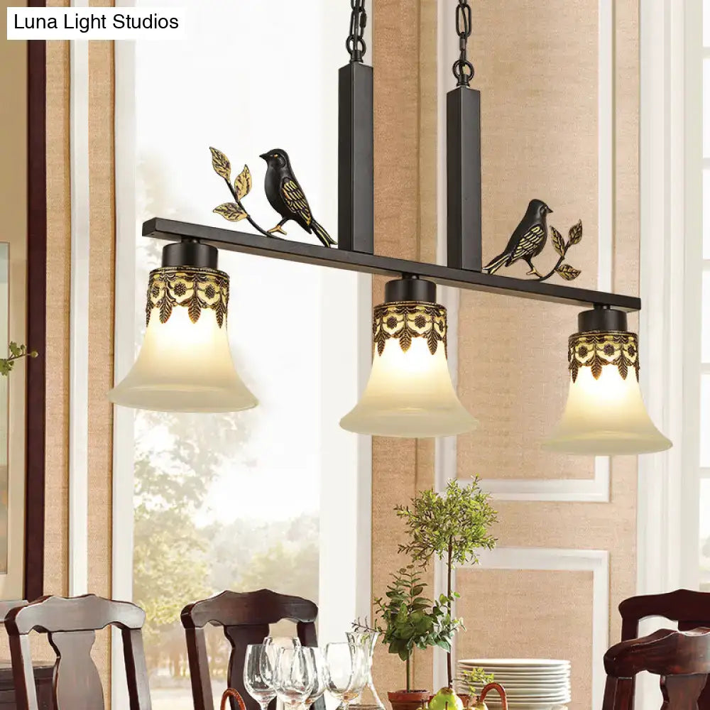 Black metal island light fixture with ornate gold detailing and three frosted glass shades featuring decorative birds
