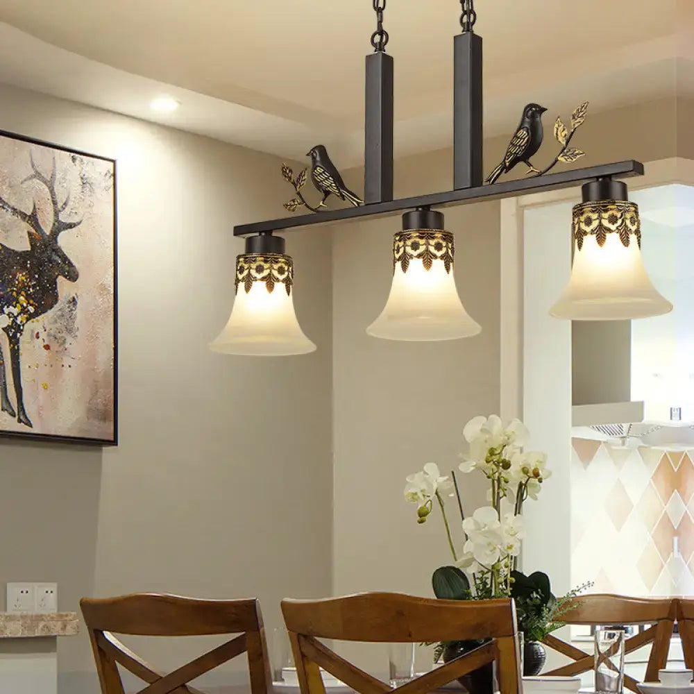 Black wrought iron island light fixture with ornate gold leaf detailing and three frosted glass bell shades