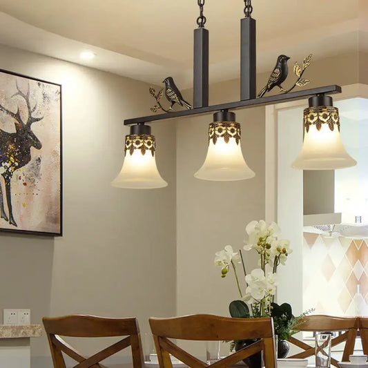 Black wrought iron island light fixture with ornate gold leaf detailing and three frosted glass bell shades