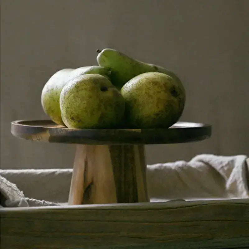 A decorbites elevated wooden cake stand set with a dark-stained top and natural wood base holding green pears