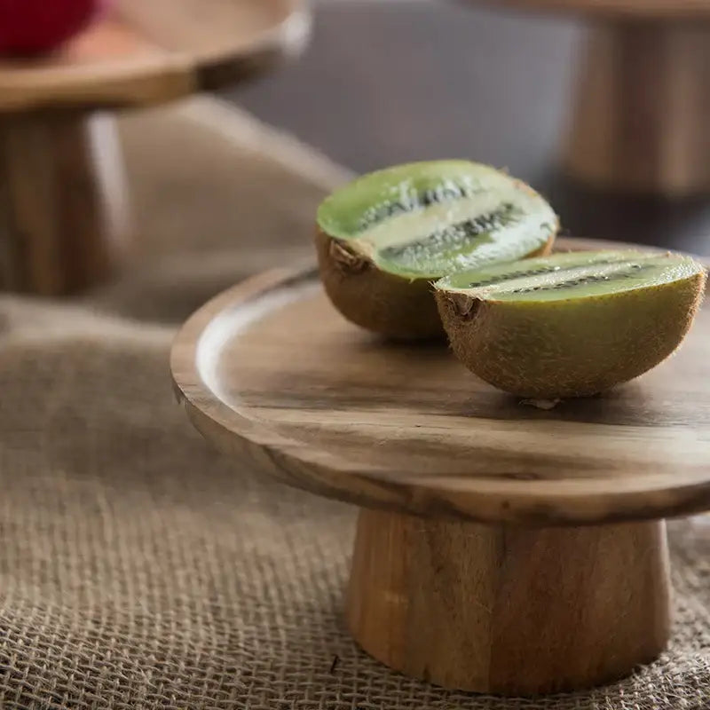 Two halves of ripe kiwi on a decorbites elevated wooden cake stand in rustic brown for dining room serving trays