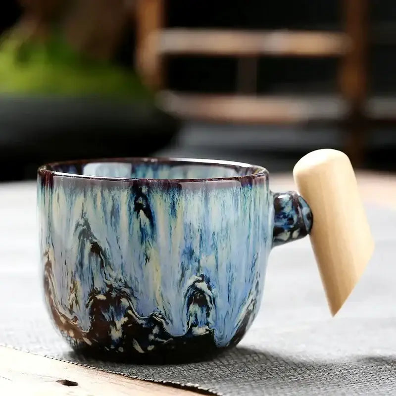 Rustic ceramic latte mug with swirling blue and black glaze and a light wood handle for kitchen drinkware