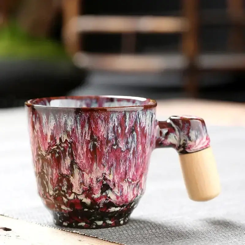Rustic glazed ceramic latte mug with vibrant red and purple swirls and a contrasting light wood handle for kitchens