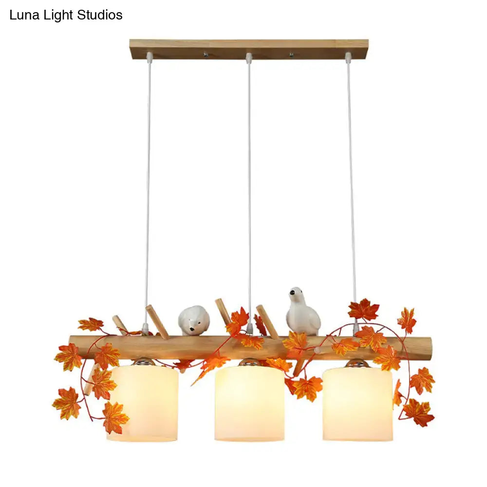 A rustic wooden island pendant light with warm glass shades featuring maple green leaf and white bird décor
