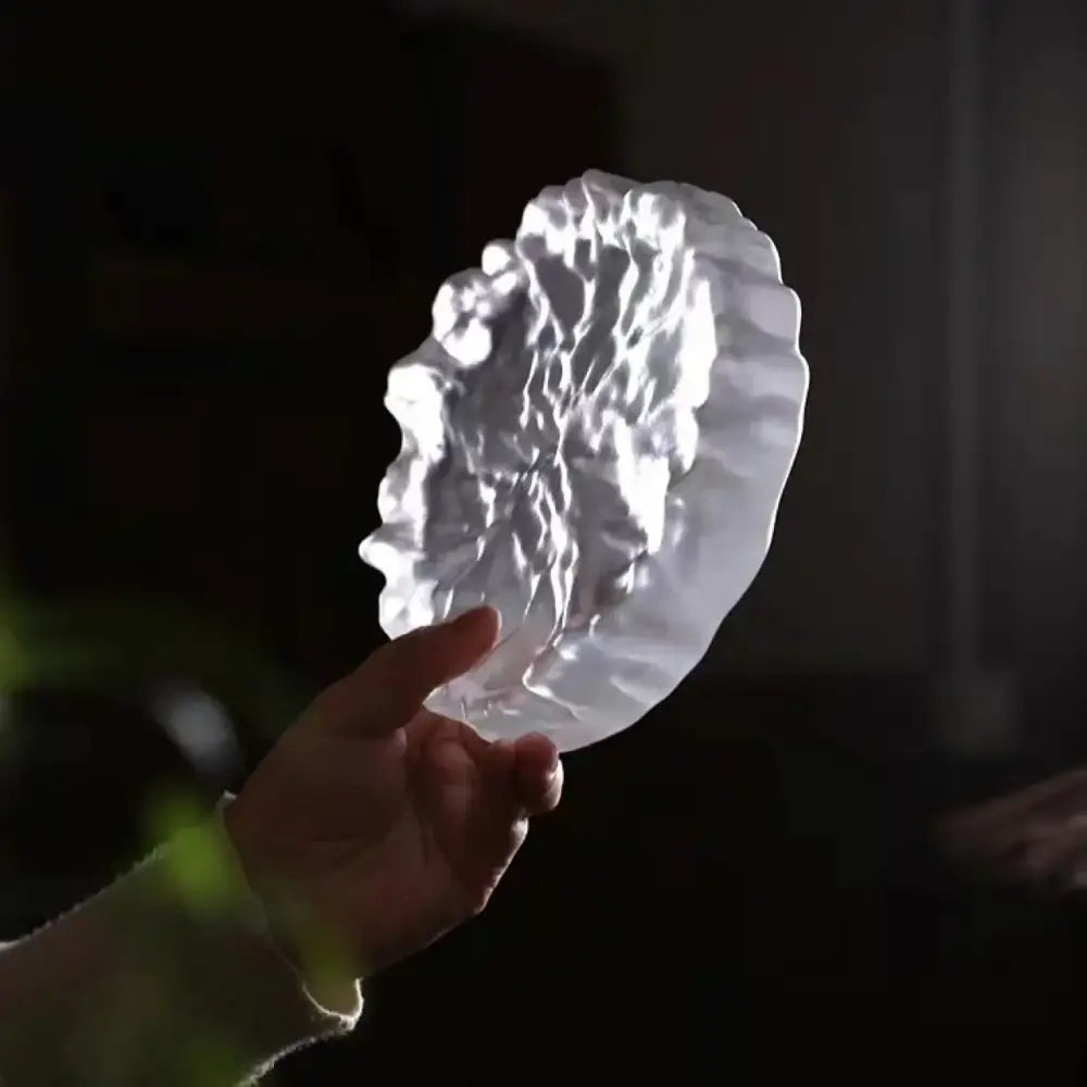 A translucent white crystal glass coaster with scalloped edges used as a minimalist jewelry display panel