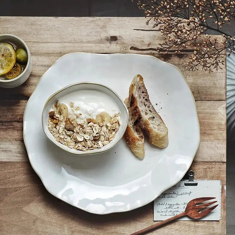 Scalloped white ceramic dinner plate set with a white ceramic bowl filled with yogurt granola and banana slices decorbites ceramic dinner