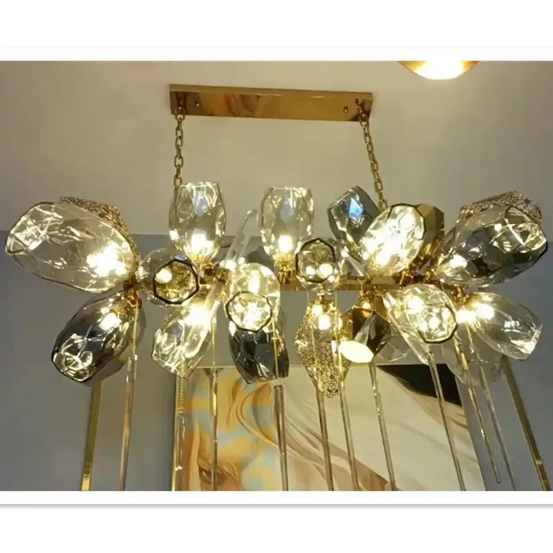 Sculptural gold pendant light with glass shades featuring faceted crystal flower elements and dangling glass rods