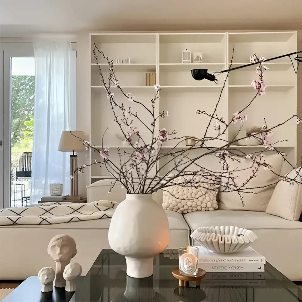 Cream-colored ceramic vase with slender curves and hammer pattern holding delicate pink blossoms for living room desk
