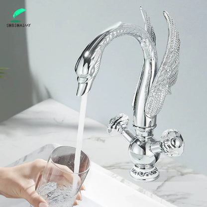 Silver swan-shaped deck mounted bathroom faucet with ornate wing detailing, crystal knobs, and cold water control