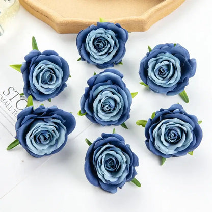 Six silk blue artificial flowers with layered petals and green stems arranged on white surface for wedding decor