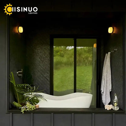 White freestanding bathtub with smooth curved design and glossy finish beside sleek gold round wall sconce glass light soap dish