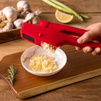 Sleek red manual press garlic crusher with a small button and black ridges crushing garlic into a white bowl by decorbites garlic crusher