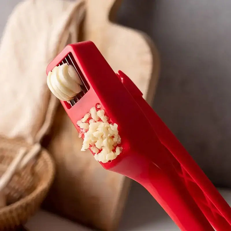 Sleek red manual decorbites garlic crusher with silicone roller mechanism and finely minced garlic residue on surface