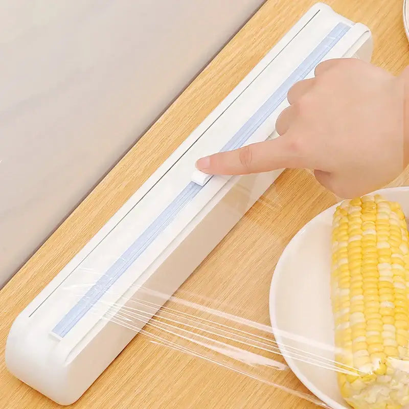 Sleek white plastic cling film dispenser cutter with light blue inner guide in use on wooden surface